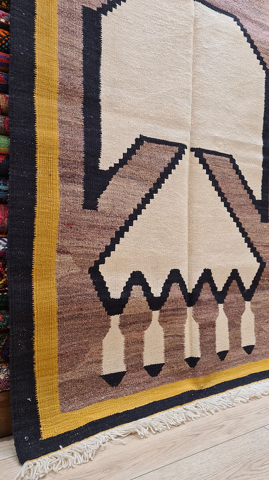 Minimalist handwoven Oushak rug with geometric bird-like figure in onyx black and desert taupe.