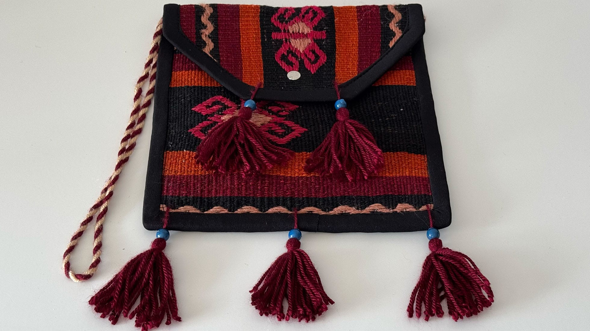 Handcrafted Kilim crossbody bag with fringes featuring tribal patterns in tangerine, fuchsia, red, and black. Made from a vintage Turkish Kilim rug with artisan fringes, this eco-friendly accessory is perfect for vibrant, boho-chic fashion lovers.