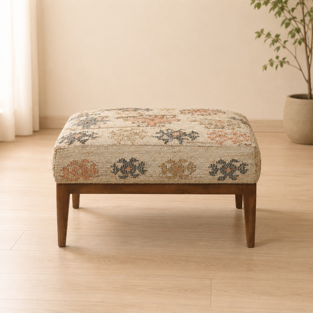 A square upholstered ottoman with a beige woven pattern and dark brown wooden legs, set in a bright, minimalist room with light wood floors and a potted plant in the background.