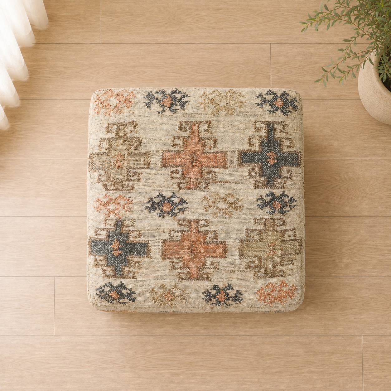 A square woven pouf ottoman with a Southwestern-style geometric pattern in beige, terracotta, and dark blue, placed on a light wood floor.