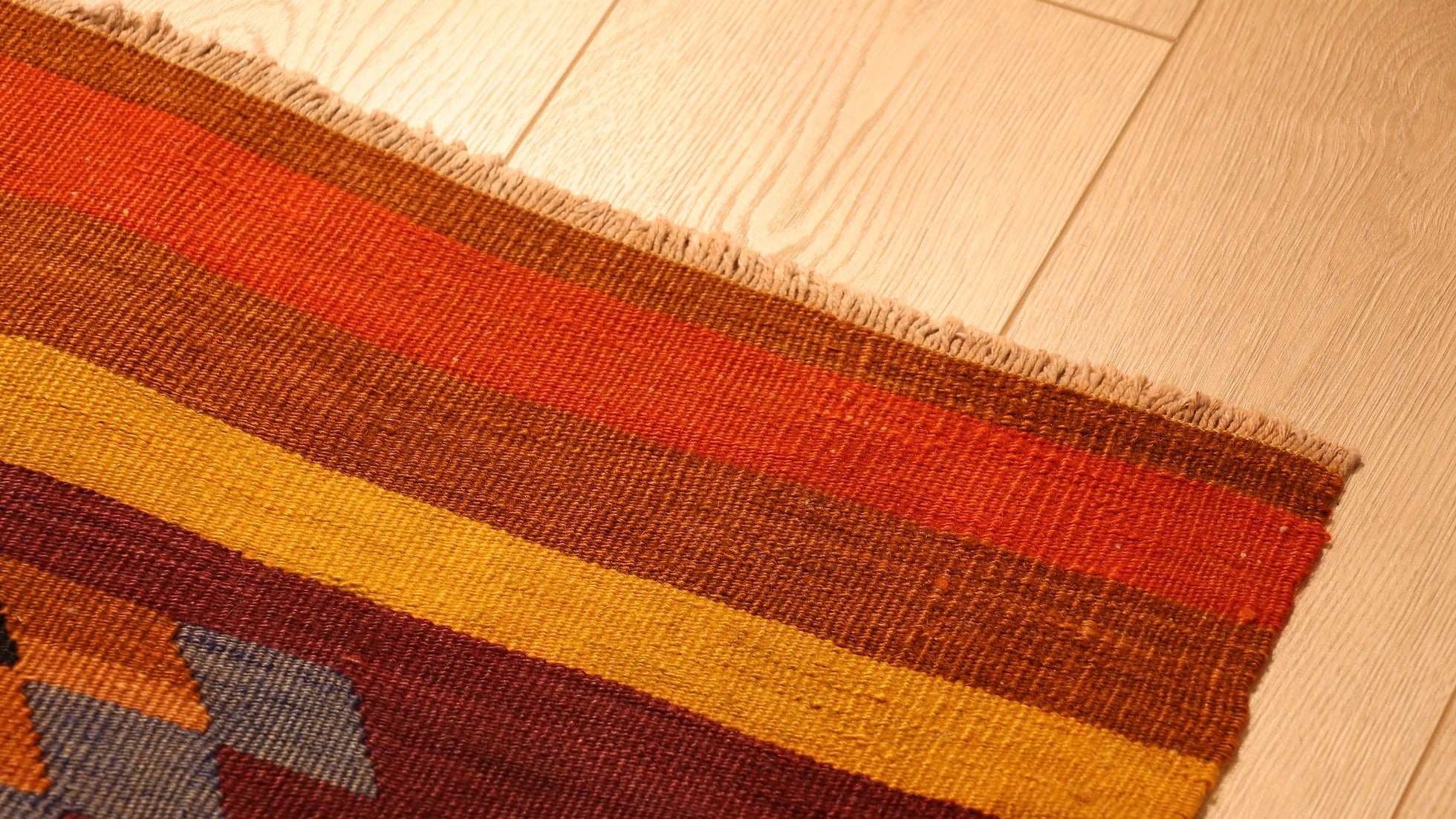 details of the edge of the vintage runner rug showcasing stripes in muted earth tones such as orange, brown, and yellow