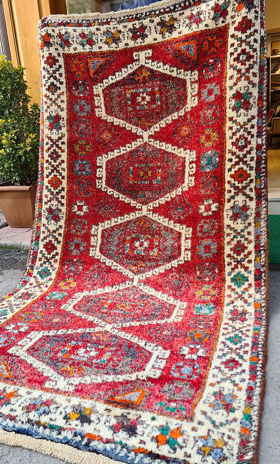 Discover the artistry of the 1970s with this Caucasian hand-knotted rug, a 5x8 ft masterpiece curated by Kilim Couture New York. Featuring a vivid crimson red base and five ivory-edged hexagonal medallions, it showcases intricate geometric and floral motifs. The striking design is framed by an ivory border adorned with vibrant hues of cobalt blue, emerald green, golden yellow, and orange, creating a balanced and versatile aesthetic.