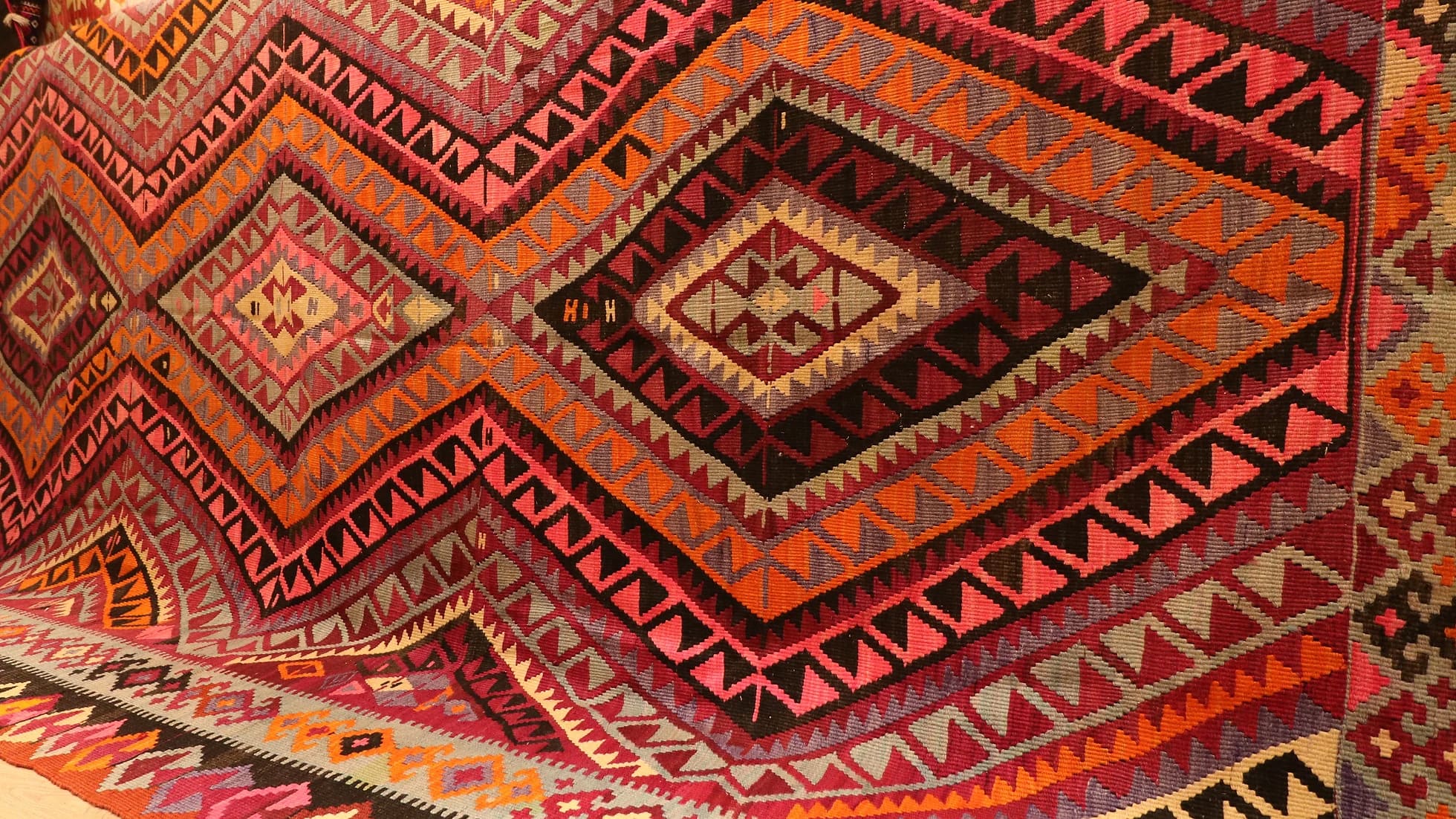 closer look at vintage handwoven flat-weave room-sized wool rug in pastel pink, red, gray, and black with diamond patterns by Kilim Couture New York