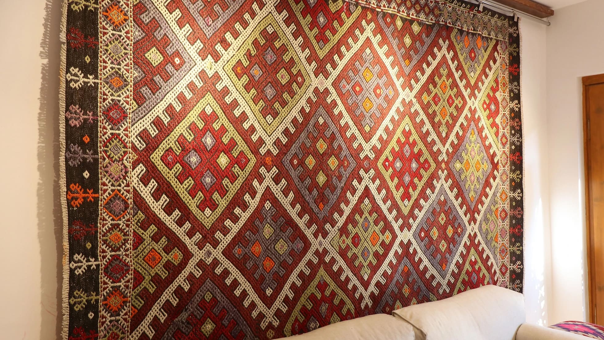 a gorgeous Turkish tribal rug featuring very rare and unseen traditional motifs in rustic and muted earth tones hanging on the wall as a Turkish tapestry from 1940s