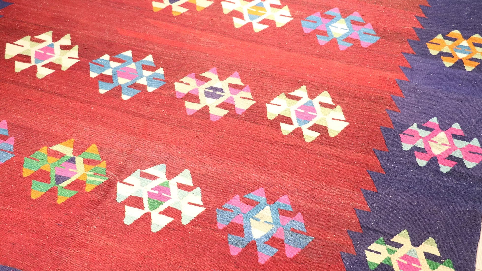 Close-up of intricate scorpion motifs in vibrant orchid fuchsia and butter yellow on a vintage Turkish handwoven kilim rug in Persian red.