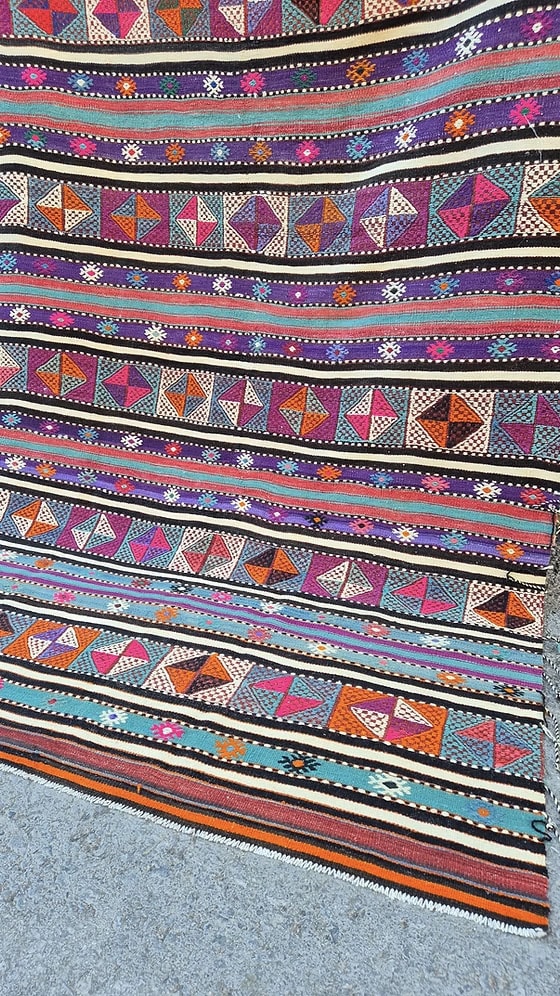 Vintage Turkish Balikesir Striped Kilim. Handwoven in the 1960s in Balikesir, this 5x8 semi-antique kilim is a rare gem of Anatolian textile heritage. Featuring bold tribal stripes and symbolic 'burdock' and 'love and unison' motifs, its inky black and ivory base is accented by plum velvet, raspberry, turquoise, and desert rose. A sophisticated yet spirited heirloom, perfect for grounding interiors with artistic depth and bohemian elegance.