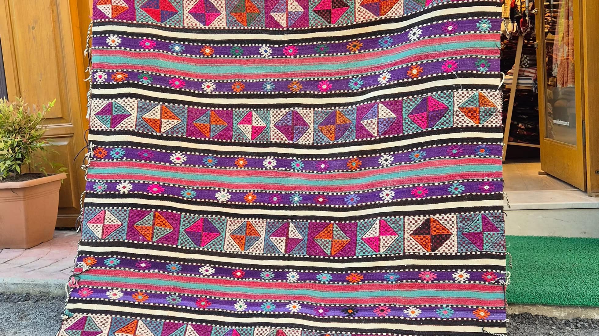 Vintage Turkish Balikesir Striped Kilim. Handwoven in the 1960s in Balikesir, this 5x8 semi-antique kilim is a rare gem of Anatolian textile heritage. Featuring bold tribal stripes and symbolic 'burdock' and 'love and unison' motifs, its inky black and ivory base is accented by plum velvet, raspberry, turquoise, and desert rose. A sophisticated yet spirited heirloom, perfect for grounding interiors with artistic depth and bohemian elegance.