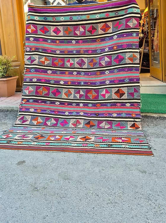 Vintage Turkish Balikesir Striped Kilim. Handwoven in the 1960s in Balikesir, this 5x8 semi-antique kilim is a rare gem of Anatolian textile heritage. Featuring bold tribal stripes and symbolic 'burdock' and 'love and unison' motifs, its inky black and ivory base is accented by plum velvet, raspberry, turquoise, and desert rose. A sophisticated yet spirited heirloom, perfect for grounding interiors with artistic depth and bohemian elegance.