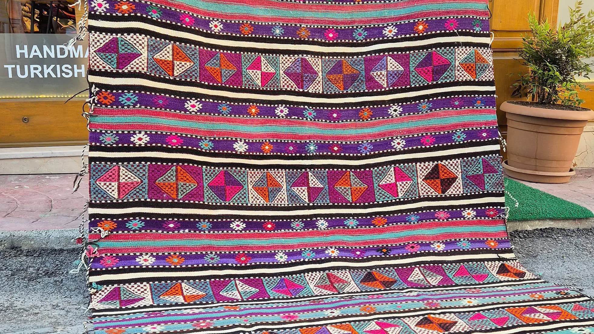 Vintage Turkish Balikesir Striped Kilim. Handwoven in the 1960s in Balikesir, this 5x8 semi-antique kilim is a rare gem of Anatolian textile heritage. Featuring bold tribal stripes and symbolic 'burdock' and 'love and unison' motifs, its inky black and ivory base is accented by plum velvet, raspberry, turquoise, and desert rose. A sophisticated yet spirited heirloom, perfect for grounding interiors with artistic depth and bohemian elegance.