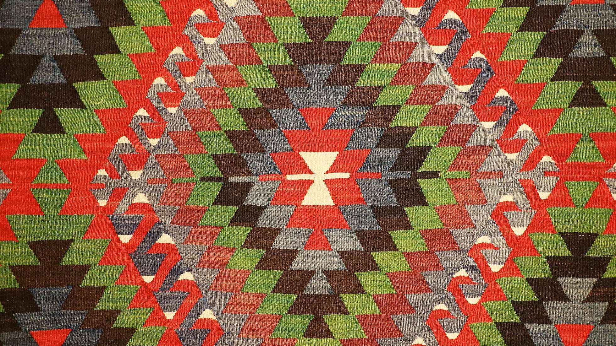 Vintage Turkish Denizli Kilim. This rare 1950s handwoven kilim from Denizli, Turkey, features a striking royal crimson backdrop with intricate 'comb' border motifs in onyx truffle and smoky gray. Measuring 6x10, its bold lozenge pattern embodies the rich craftsmanship of Anatolian weaving. A timeless fusion of history and elegance, this versatile heirloom rug adds warmth and sophistication to any space.