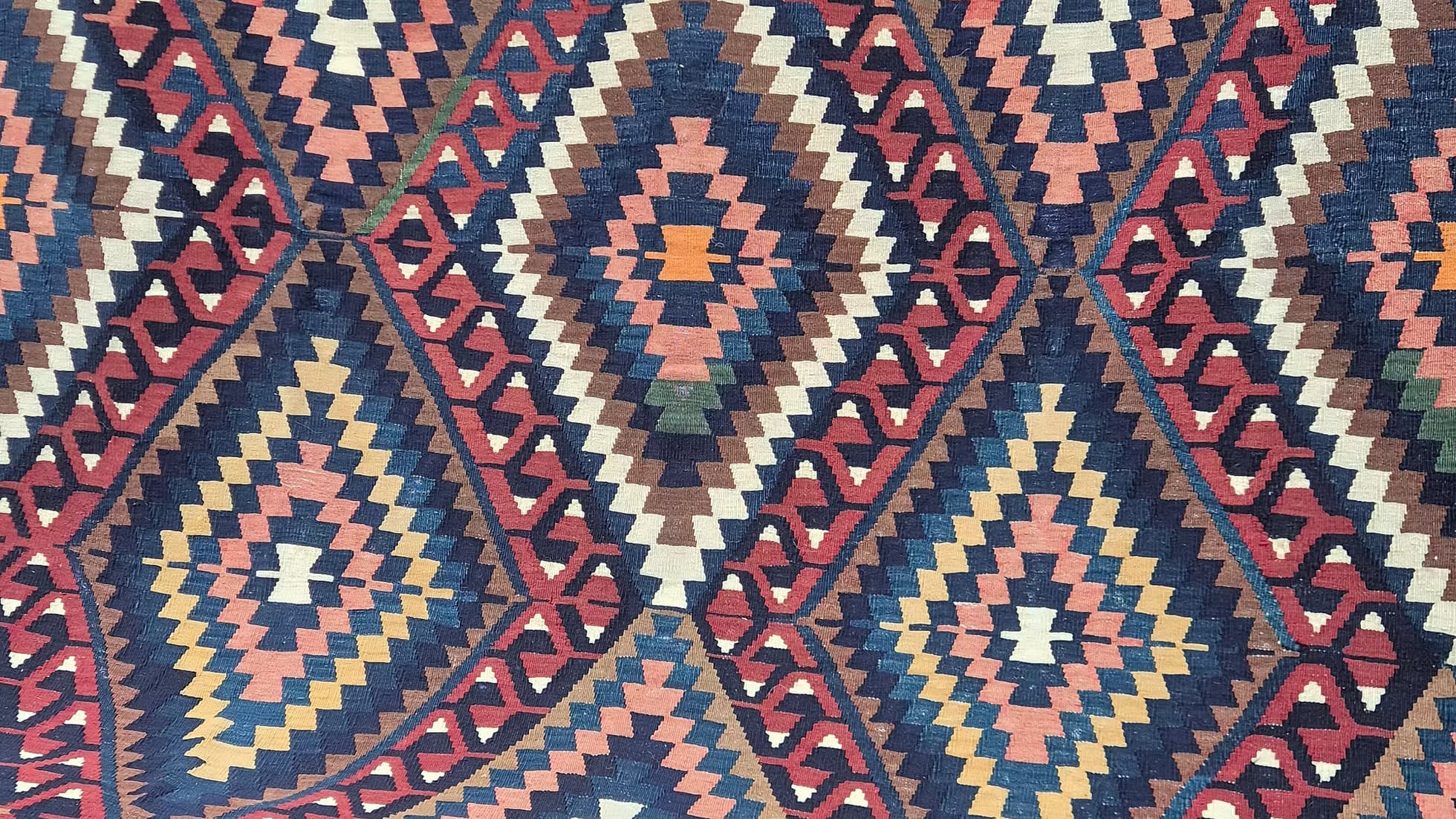 Close-up of a diamond patterned Turkish rug with geometric design in red, blue, and beige.