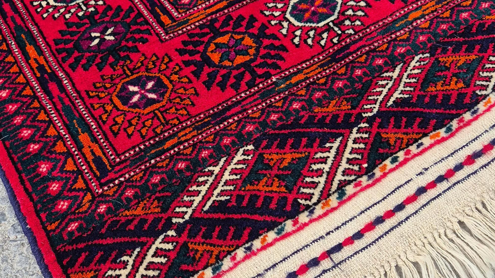 Details of a Central Asian Turkmen Bokhara rug in saturated crimson and coral tones with traditional gul medallions,