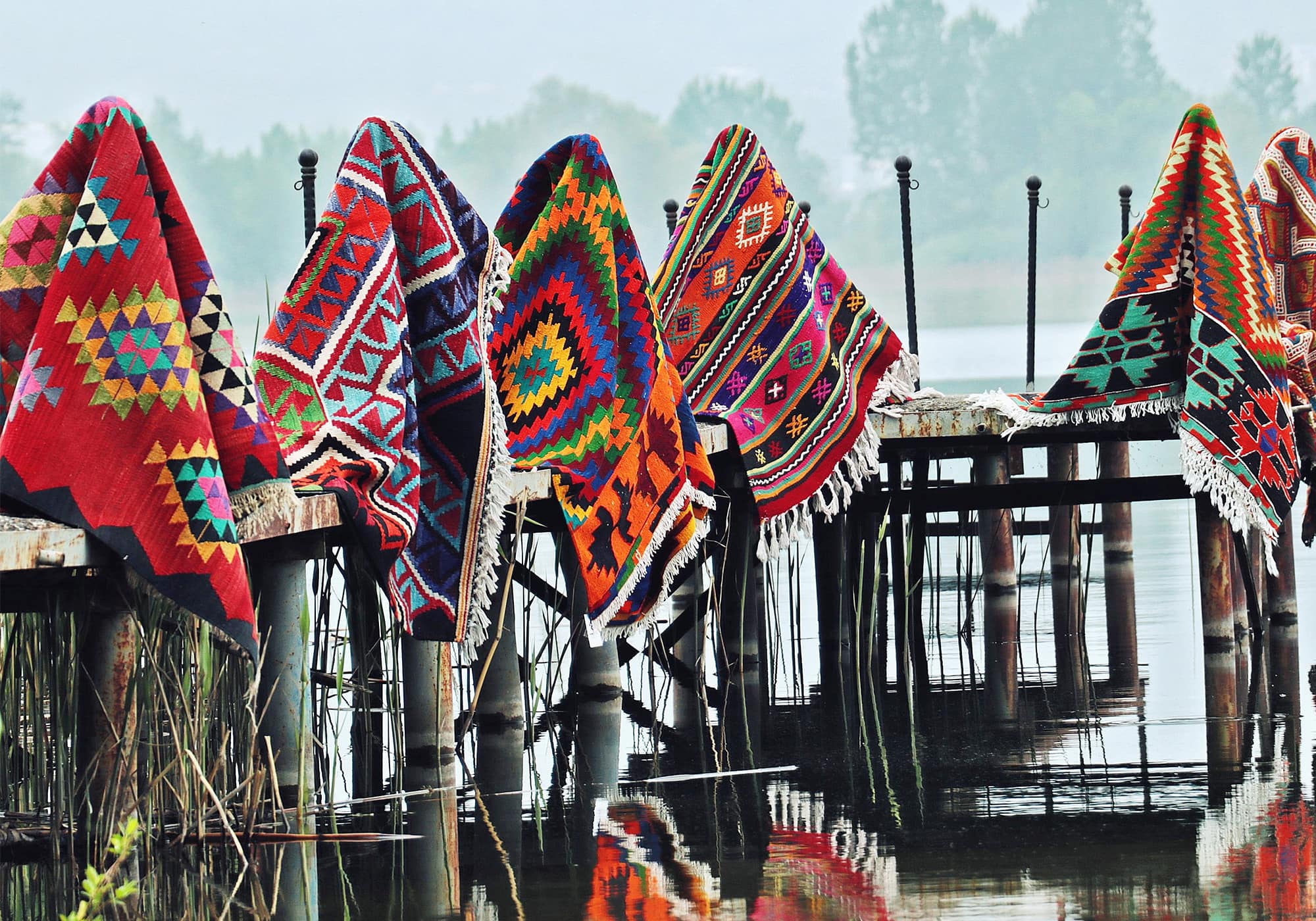 Various types of antique and vintage Turkish rugs and kilims are being displayed against the backdrop of a picturesque Turkish setting