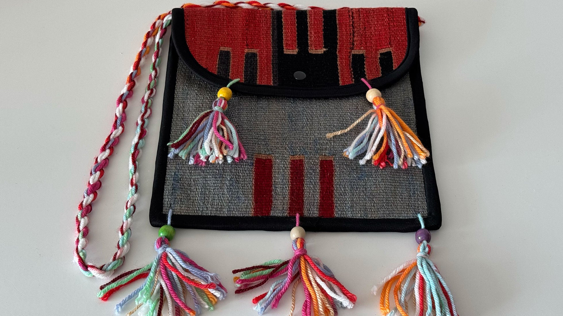 Handcrafted Kilim crossbody bag featuring tribal patterns in black, red, and grayish denim. Made from a vintage Turkish Kilim rug, with artisan fringes and an eco-friendly design—perfect for New York fashion enthusiasts and sustainable style lovers.