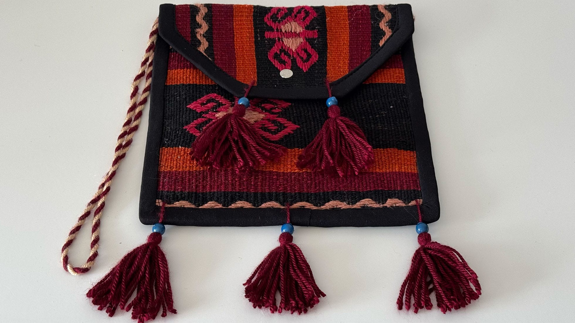 Handcrafted Kilim crossbody bag with fringes featuring tribal patterns in tangerine, fuchsia, red, and black. Made from a vintage Turkish Kilim rug with artisan fringes, this eco-friendly accessory is perfect for vibrant, boho-chic fashion lovers.
