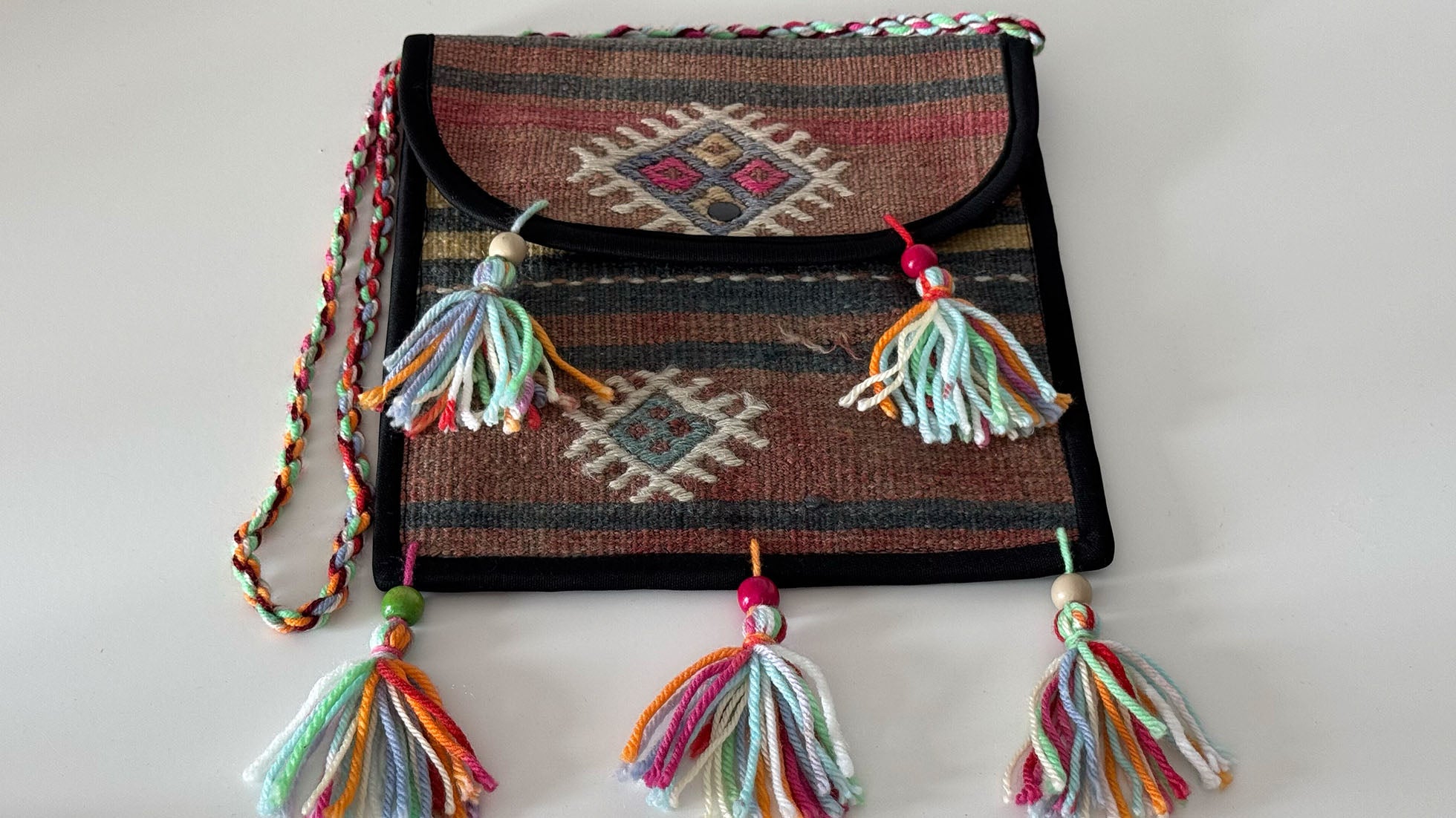 Polychromatic handcrafted Kilim crossbody bag featuring tribal patterns in pastel pink, gray, white, and earthy sand. Made from a vintage Turkish Kilim rug, this eco-friendly accessory combines traditional craftsmanship with a modern, refined aesthetic.