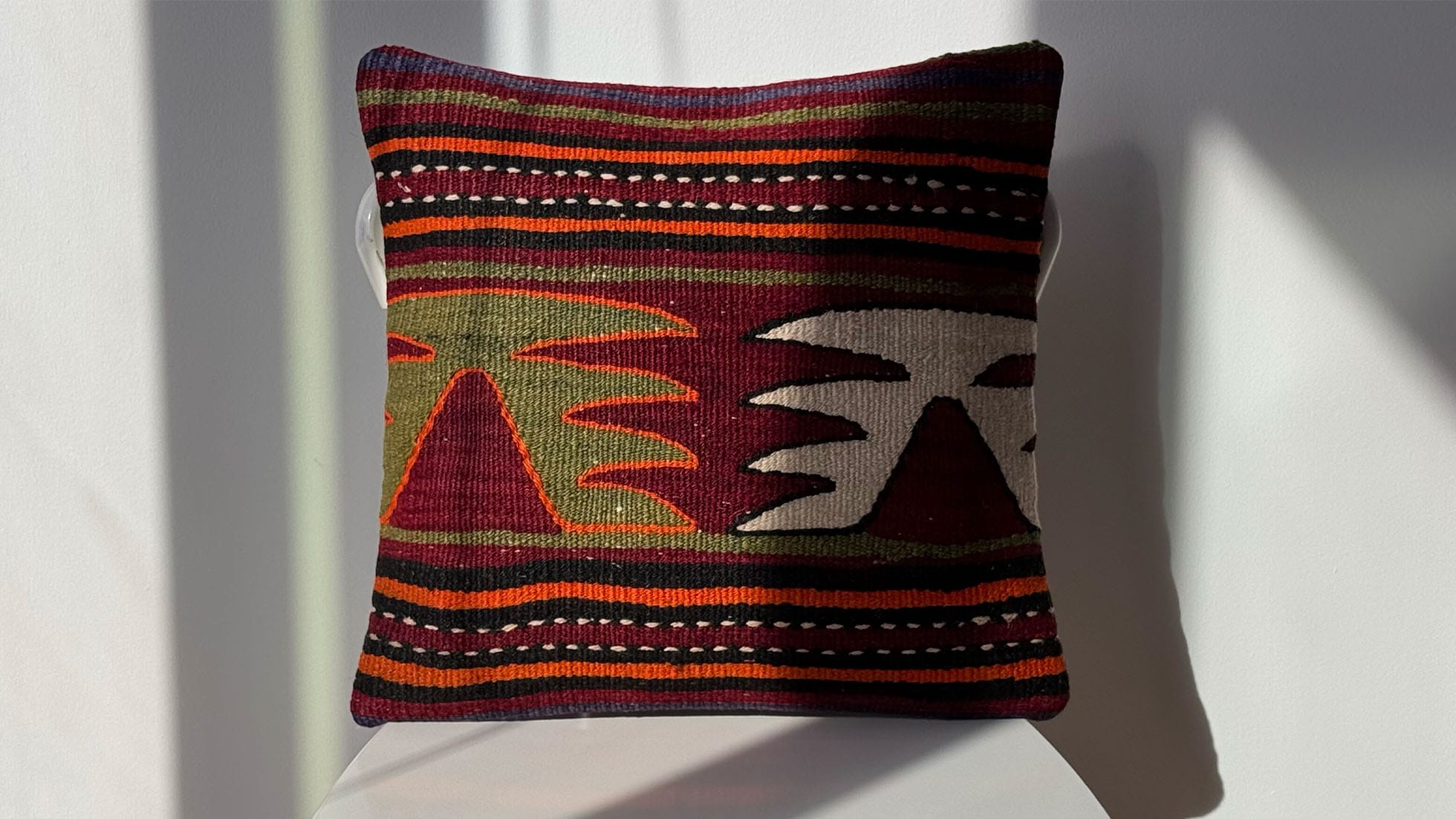 Vintage handwoven kilim pillow in burgundy with orange, green, and black stripes and tribal motifs in khaki and white, handcrafted by Kilim Couture New York. Ideal for home decor, rustic, contemporary, and mid-century modern interiors. Decorative throw pillow, handwoven Turkish rug cushion, unique accent pillow, sustainable luxury home accessory.