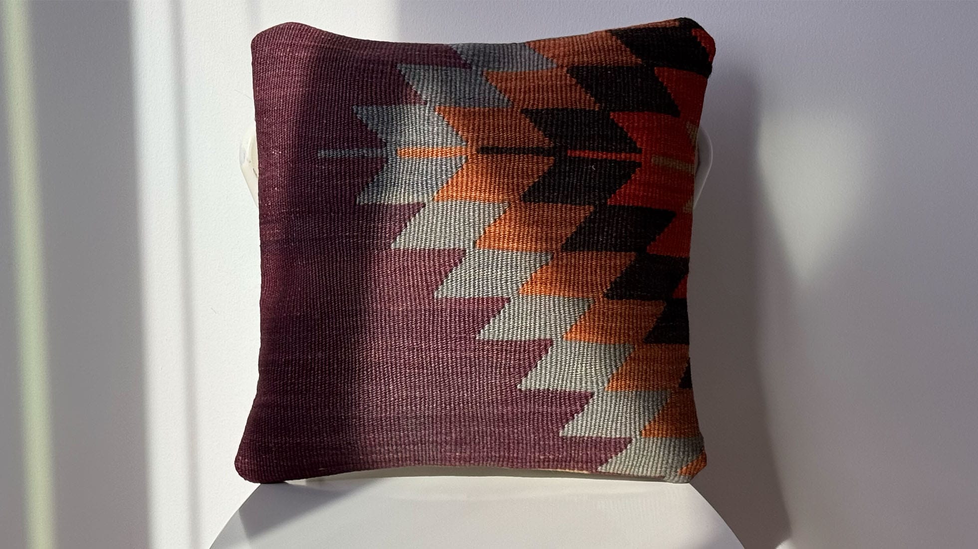 One-of-a-kind 16x16 vintage handwoven kilim pillow with intricate geometric diamond patterns in deep plum, terracotta, and charcoal, handcrafted from a semi-antique Turkish kilim rug, adding a touch of rustic elegance and warmth to any interior space.