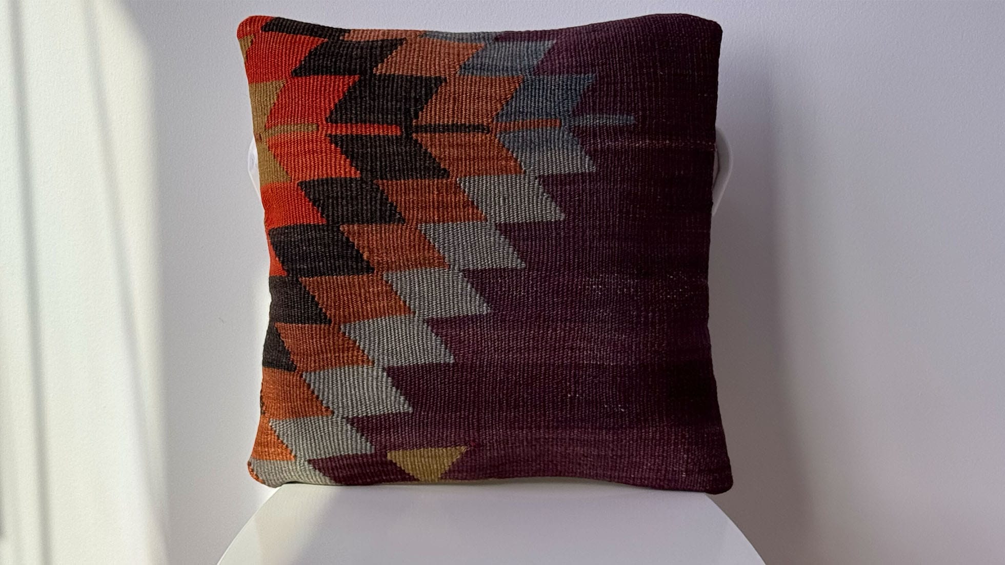 Vintage handwoven kilim pillow with geometric diamond patterns in deep plum, terracotta, and charcoal. This unique, antique Turkish rug cushion adds rustic elegance and warmth to bohemian, eclectic, or modern interiors. Perfect for interior designers in NYC seeking a textured, one-of-a-kind decorative throw pillow to elevate their projects.