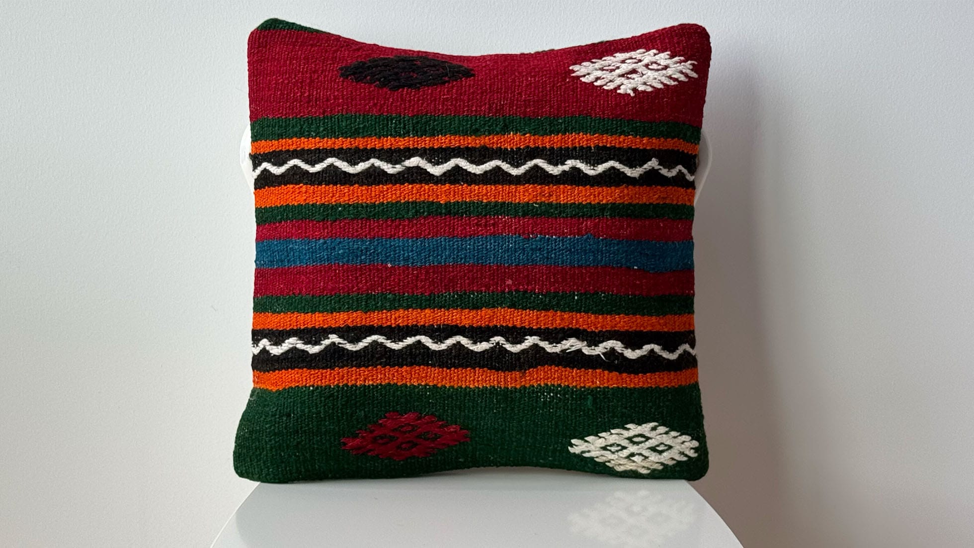 Handwoven Vintage Turkish Kilim Pillow—Unique artisan decorative throw pillow featuring bold geometric patterns and stripes in red, orange, black, green colors, ideal for interior design projects. Perfect for adding cultural charm and sophistication to boho, eclectic, or rustic interiors, handcrafted from mid-century kilim fragments for a one-of-a-kind statement piece.