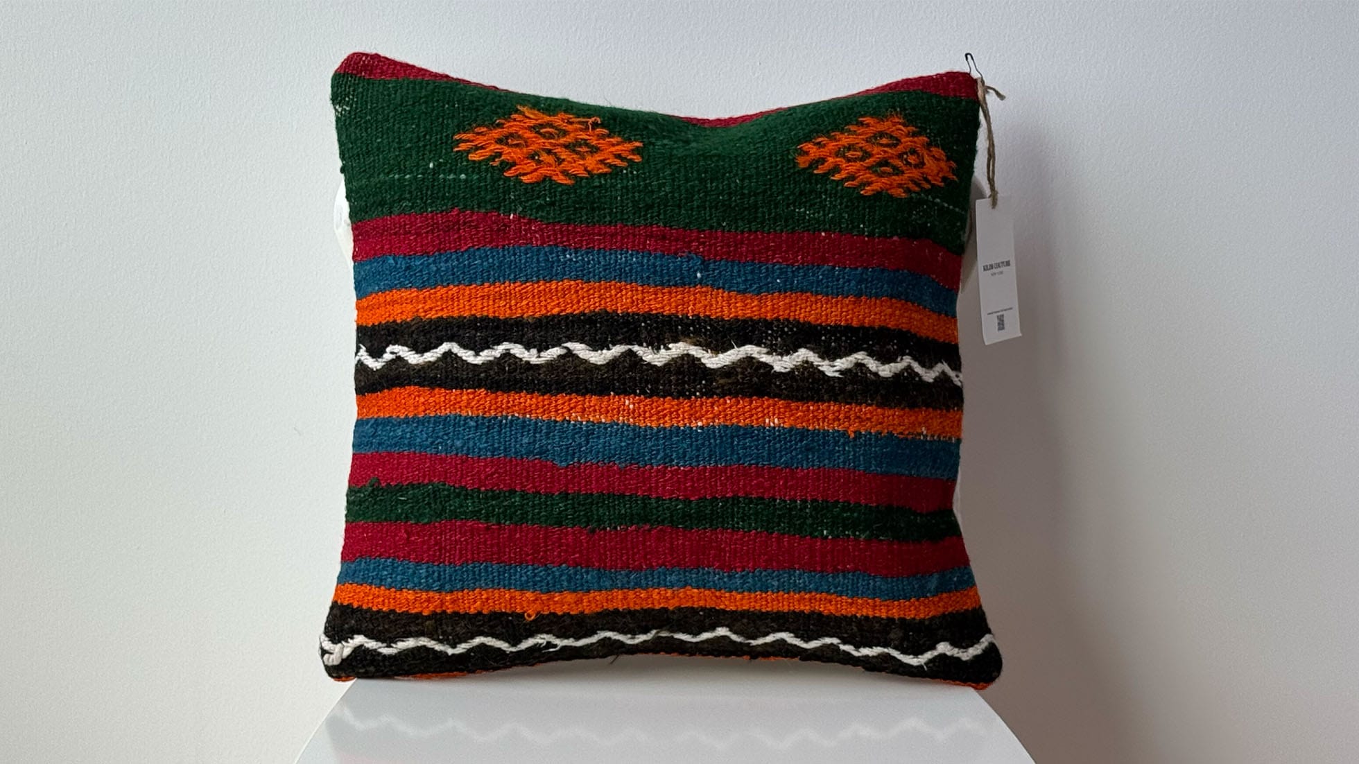 Vintage Turkish kilim pillow with earthy green, orange, and blue hues, featuring intricate burdock motifs, geometric stripes, and flowing black accents. Handcrafted from mid-century kilim fragments by skilled artisans, perfect for adding cultural depth and luxury to designer interiors.