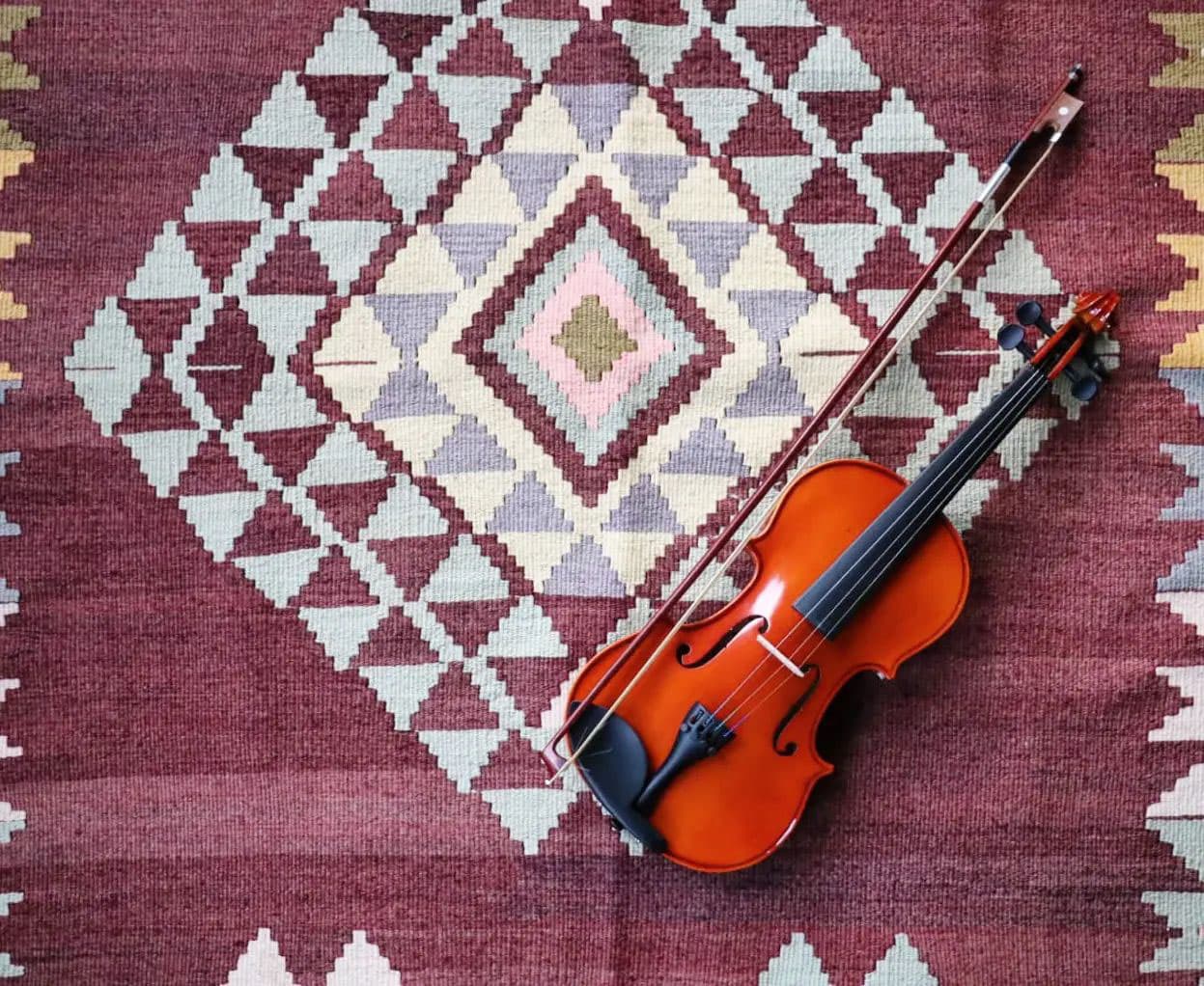 A rich, earth-toned kilim with a traditional diamond motif, elegantly paired with a classic violin resting on its textured surface.