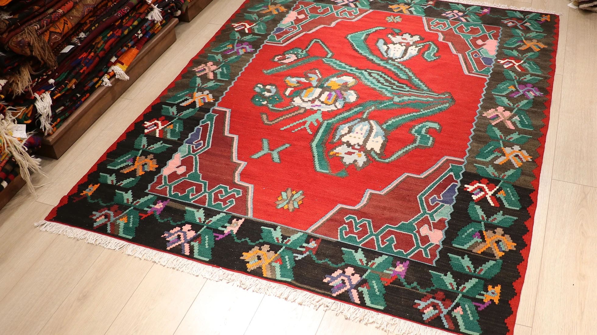 Handwoven vintage Bessarabian kilim rug, 5x7 ft, with a bold oriental red backdrop featuring intricate floral bouquets in cream, aqua green, purple, and lush green foliage, framed by a faded black border with floral accents, showcasing mid-20th century craftsmanship and European elegance.