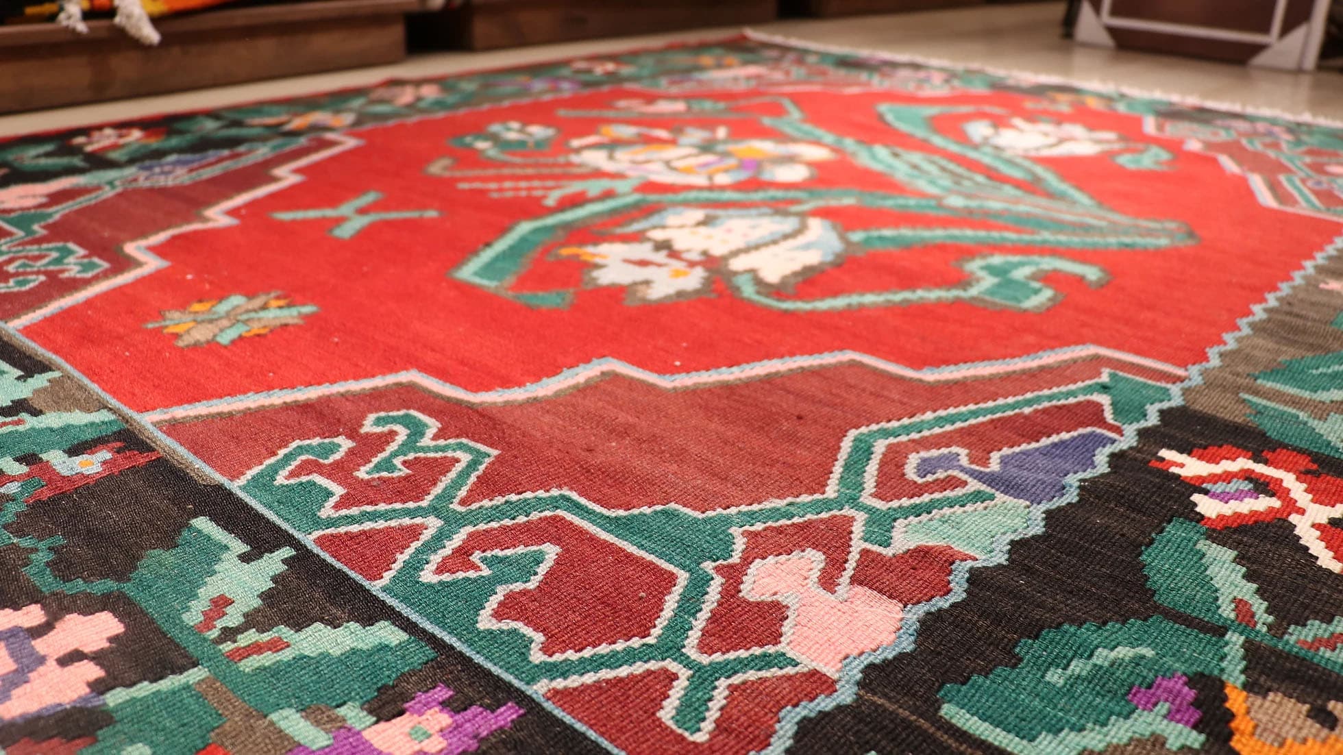 Handwoven vintage Bessarabian kilim rug, 5x7 ft, with a bold oriental red backdrop featuring intricate floral bouquets in cream, aqua green, purple, and lush green foliage, framed by a faded black border with floral accents, showcasing mid-20th century craftsmanship and European elegance.