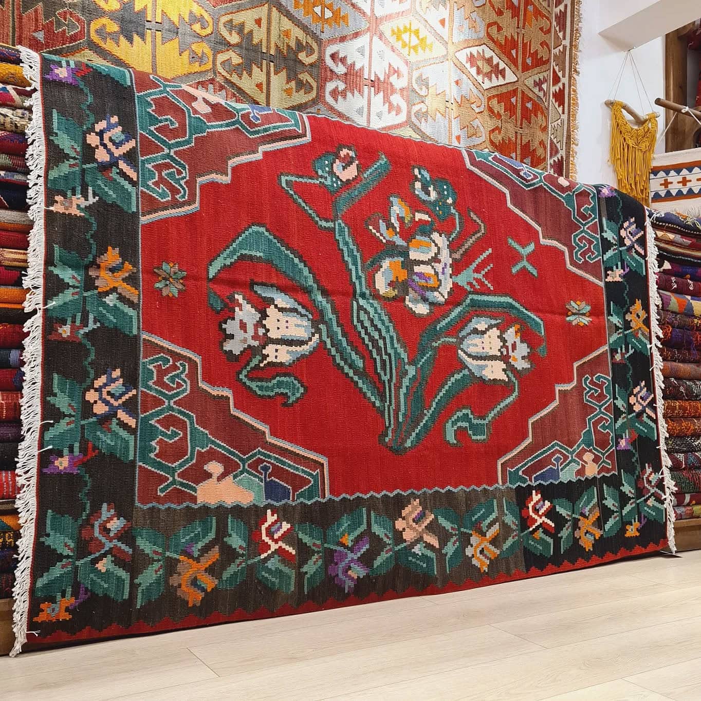 Handwoven vintage Bessarabian kilim rug, 5x7 ft, with a bold oriental red backdrop featuring intricate floral bouquets in cream, aqua green, purple, and lush green foliage, framed by a faded black border with floral accents, showcasing mid-20th century craftsmanship and European elegance.