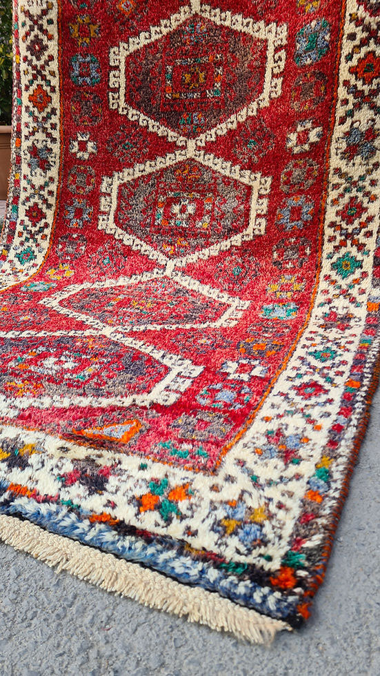 Discover the artistry of the 1970s with this Caucasian hand-knotted rug, a 5x8 ft masterpiece curated by Kilim Couture New York. Featuring a vivid crimson red base and five ivory-edged hexagonal medallions, it showcases intricate geometric and floral motifs. The striking design is framed by an ivory border adorned with vibrant hues of cobalt blue, emerald green, golden yellow, and orange, creating a balanced and versatile aesthetic.