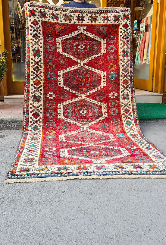 Discover the artistry of the 1970s with this Caucasian hand-knotted rug, a 5x8 ft masterpiece curated by Kilim Couture New York. Featuring a vivid crimson red base and five ivory-edged hexagonal medallions, it showcases intricate geometric and floral motifs. The striking design is framed by an ivory border adorned with vibrant hues of cobalt blue, emerald green, golden yellow, and orange, creating a balanced and versatile aesthetic.
