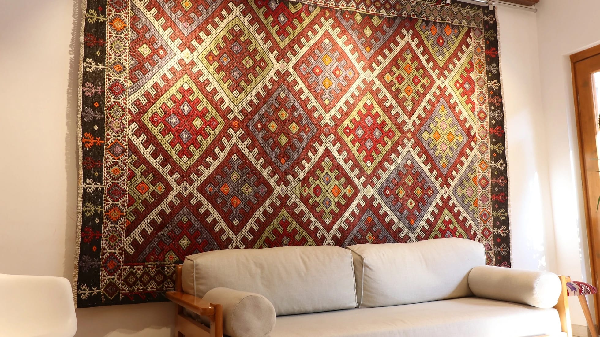 a gorgeous Turkish tribal rug featuring very rare and unseen traditional motifs in rustic and muted earth tones hanging on the wall as a Turkish tapestry from 1940s