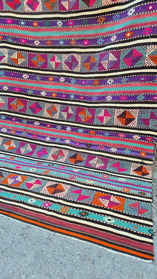 Vintage Turkish Balikesir Striped Kilim. Handwoven in the 1960s in Balikesir, this 5x8 semi-antique kilim is a rare gem of Anatolian textile heritage. Featuring bold tribal stripes and symbolic 'burdock' and 'love and unison' motifs, its inky black and ivory base is accented by plum velvet, raspberry, turquoise, and desert rose. A sophisticated yet spirited heirloom, perfect for grounding interiors with artistic depth and bohemian elegance.