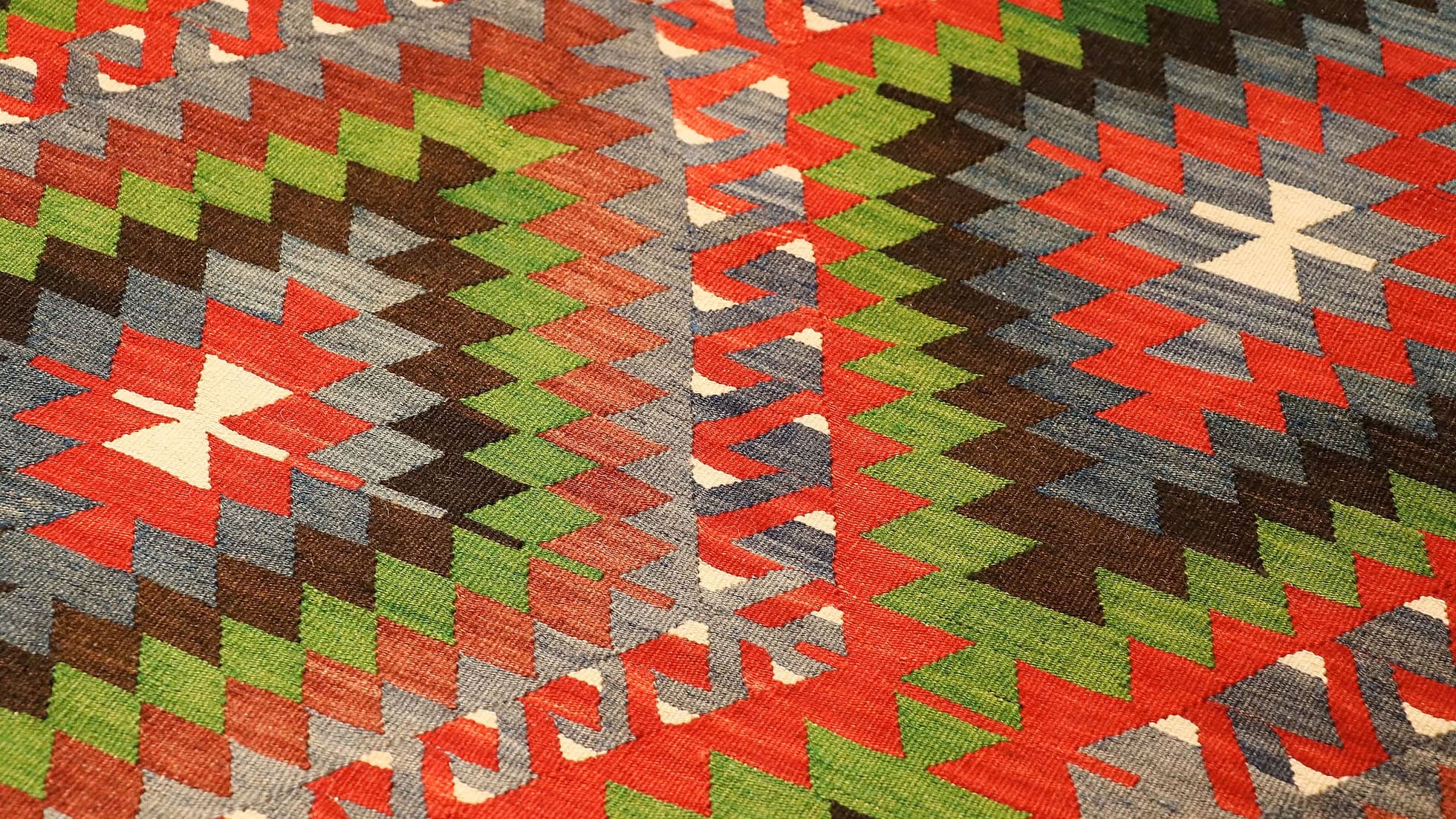 Vintage Turkish Denizli Kilim. This rare 1950s handwoven kilim from Denizli, Turkey, features a striking royal crimson backdrop with intricate 'comb' border motifs in onyx truffle and smoky gray. Measuring 6x10, its bold lozenge pattern embodies the rich craftsmanship of Anatolian weaving. A timeless fusion of history and elegance, this versatile heirloom rug adds warmth and sophistication to any space.