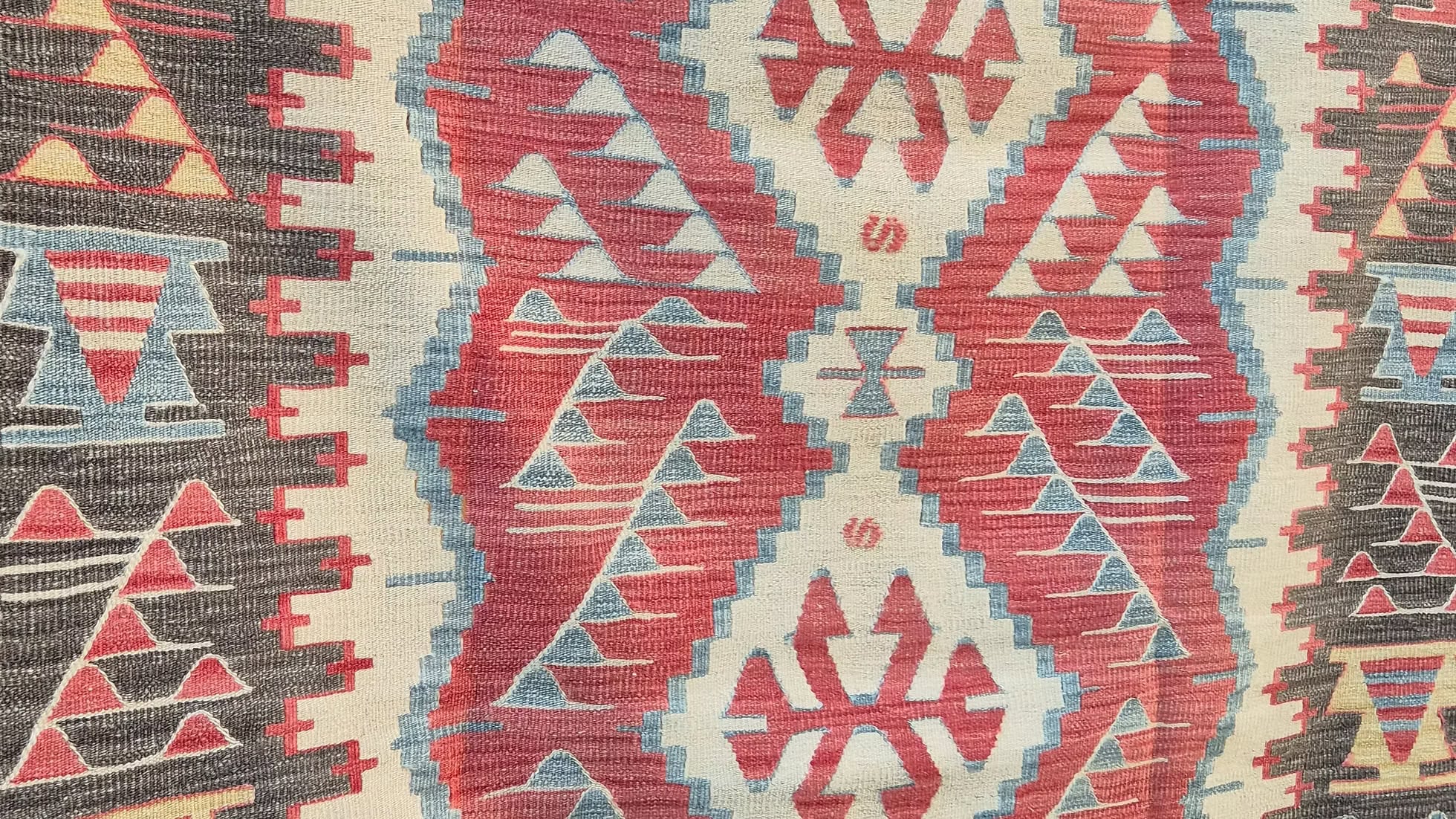 Close-up of a rustic patterned rug with geometric designs in red, beige, and blue by Kilim Couture New York Rug Gallery.